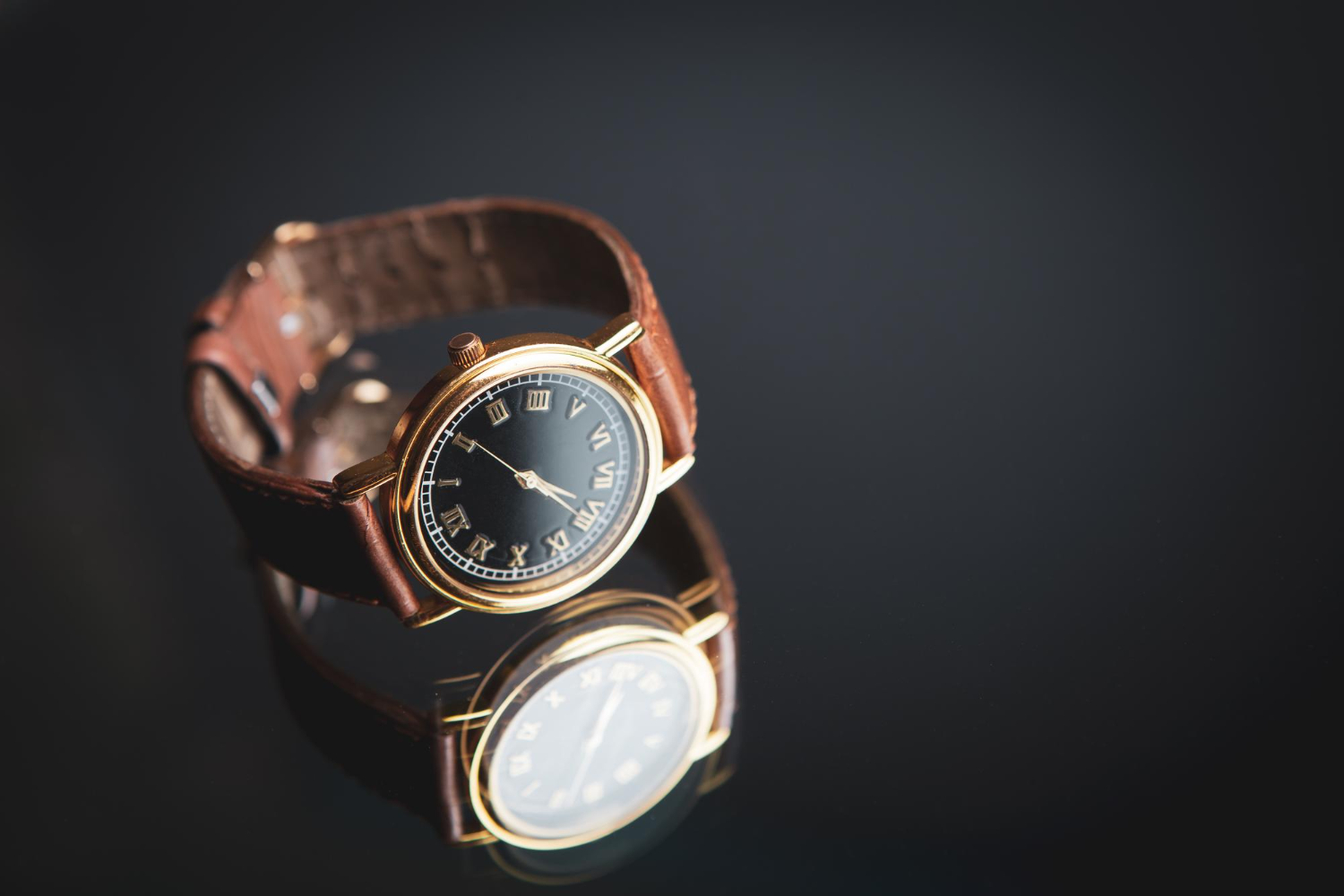 black dial watch with gold roman numerals and a brown leather strap